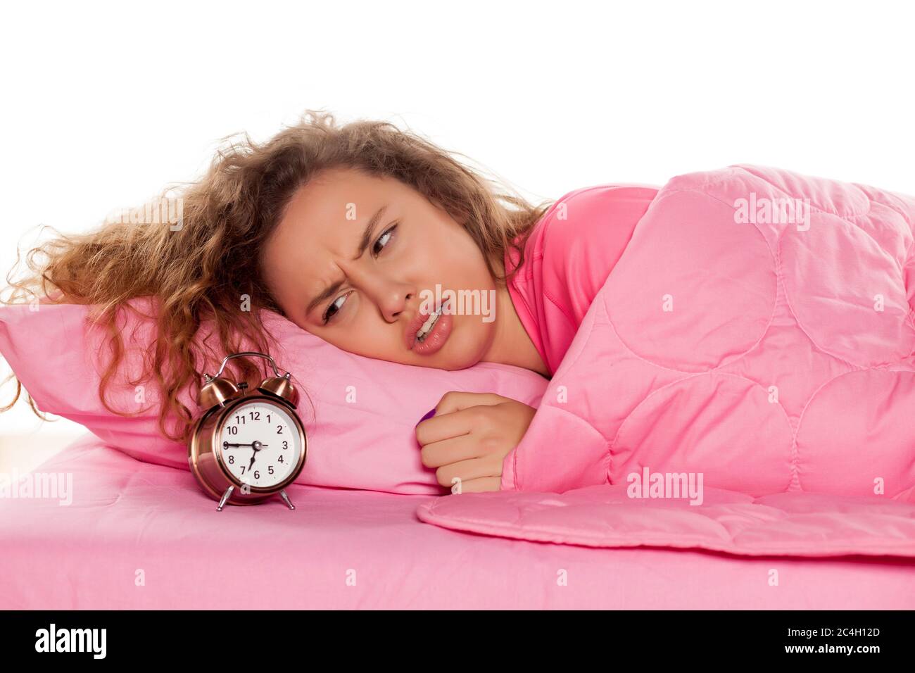 une jeune femme nerveuse se réveille avec un réveil sur fond blanc Banque D'Images