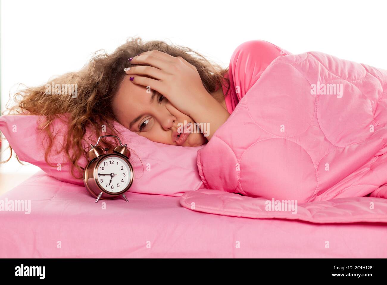 une jeune femme nerveuse se réveille avec un réveil sur fond blanc Banque D'Images