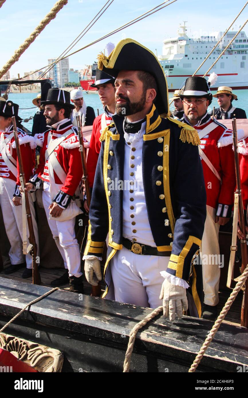 Malaga, Espagne - 26 octobre 2014 : capitaine de la Marine royale du XVIIIe siècle à bord d'un navire avec son équipage. Les gens derrière avec l'uniforme de marine royale, co rouge Banque D'Images
