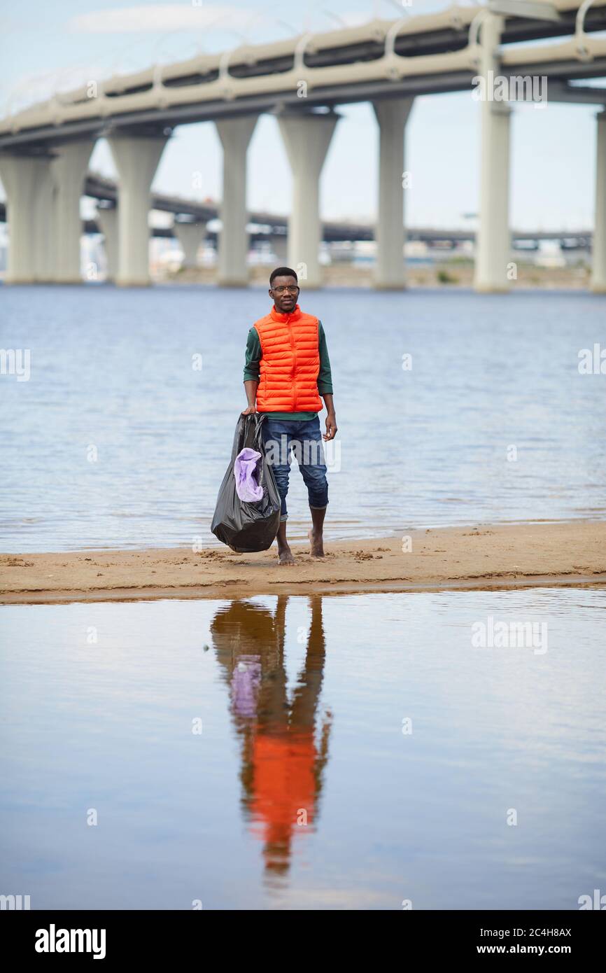 Portrait d'un jeune africain debout avec des ordures sur la rive de la rivière avec un grand pont en arrière-plan Banque D'Images