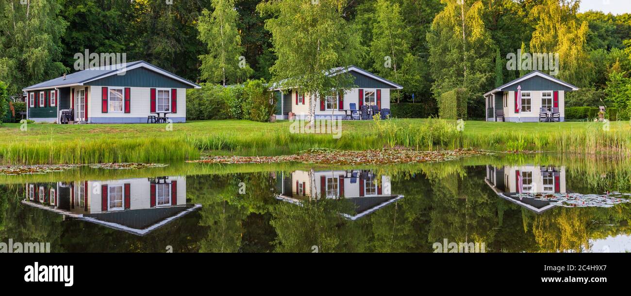 Panorama avec rangée de maisons de vacances en bois colorées se reflète dans un étang au parc de loisirs au milieu de la nature aux pays-Bas Banque D'Images