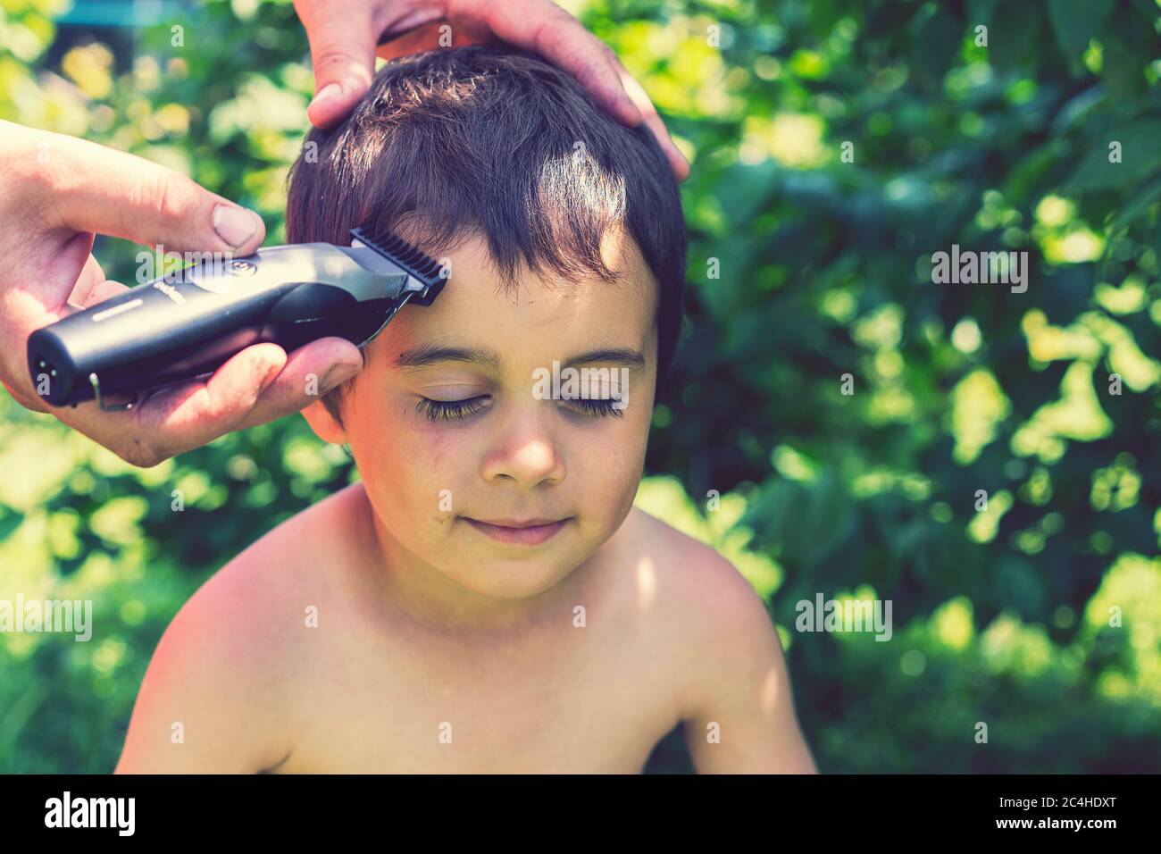 main tient une tondeuse à cheveux électrique et coupe les cheveux longs du  garçon, barbershop à la maison, parent coupe les cheveux pendant que les  coiffeurs sont fermés, rester à la maison