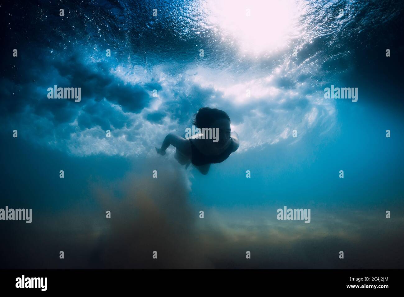 Femme plongée sans planche de surf sous la vague de l'océan. Plongée sous-marine en canard sous les vagues et fond sablonneux Banque D'Images