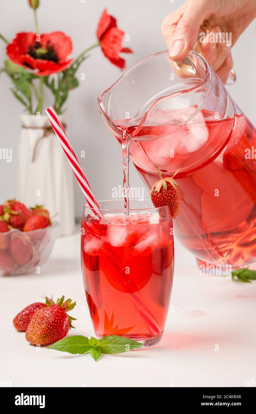 Une femme verse une boisson rafraîchissante d'été avec des fraises et de la glace à partir d'un détanter. Photo verticale Banque D'Images