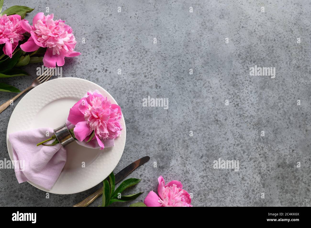 Table festive avec pivoine rose, vaisselle blanche, couverts gris. Vue de dessus. Banque D'Images