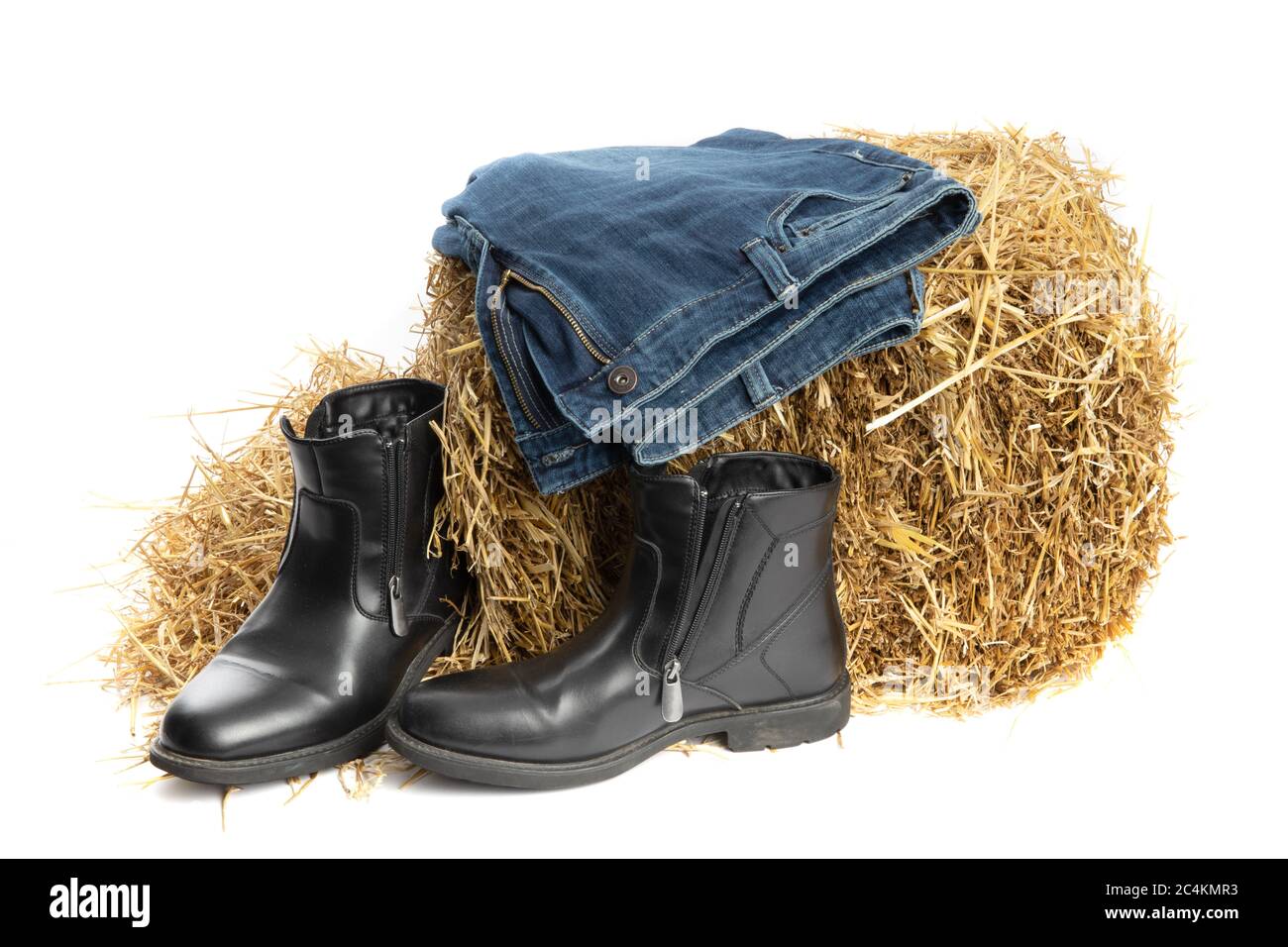 mode agricole, jeans en denim bleu et bottes en cuir noir sur une balle de foin dans une grange isolée sur blanc Banque D'Images