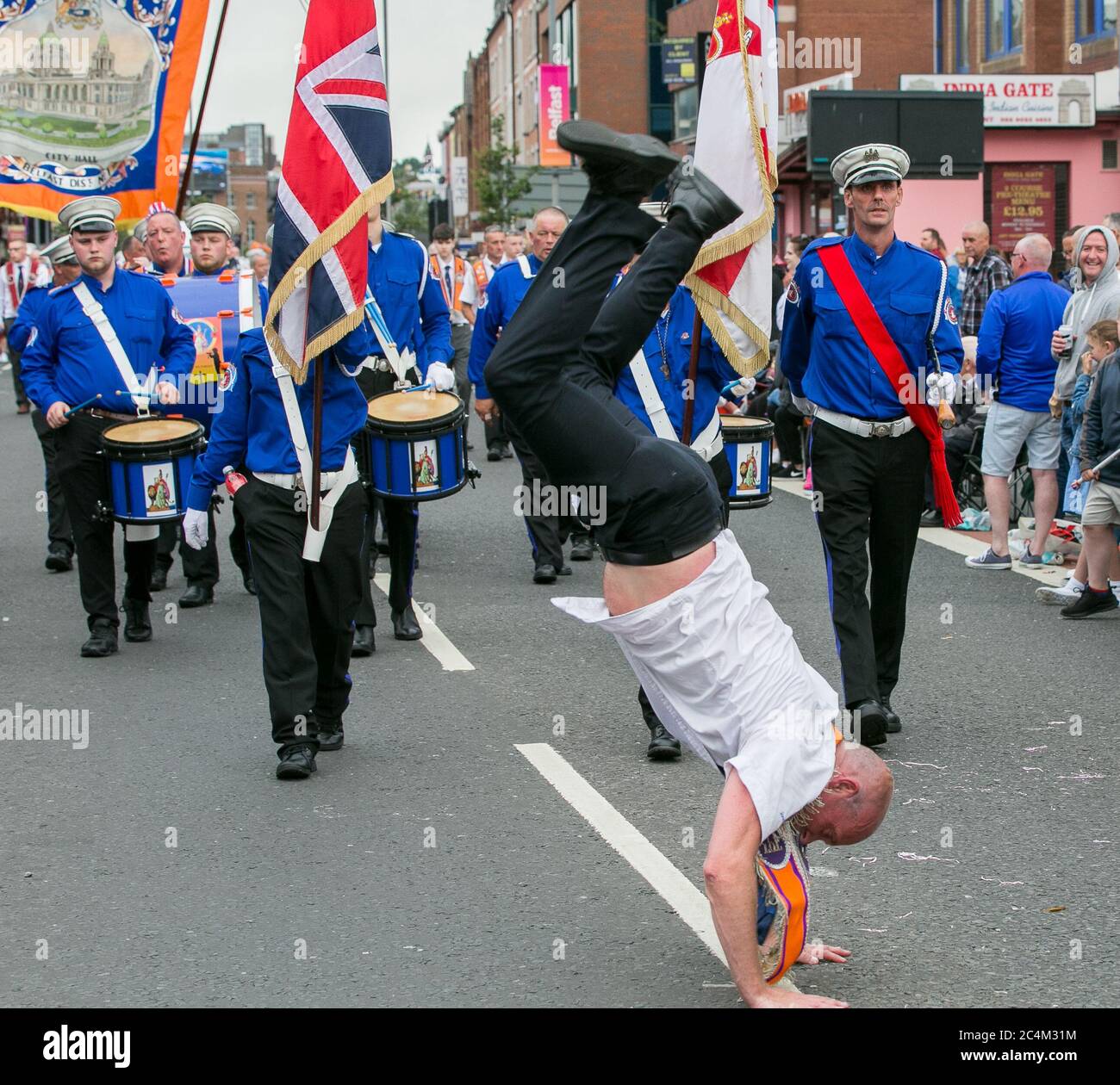 Danse dans la rue 12e (douzième) juillet Parade, Belfast. Homme faisant une main dans la rue devant un groupe de marche. Banque D'Images