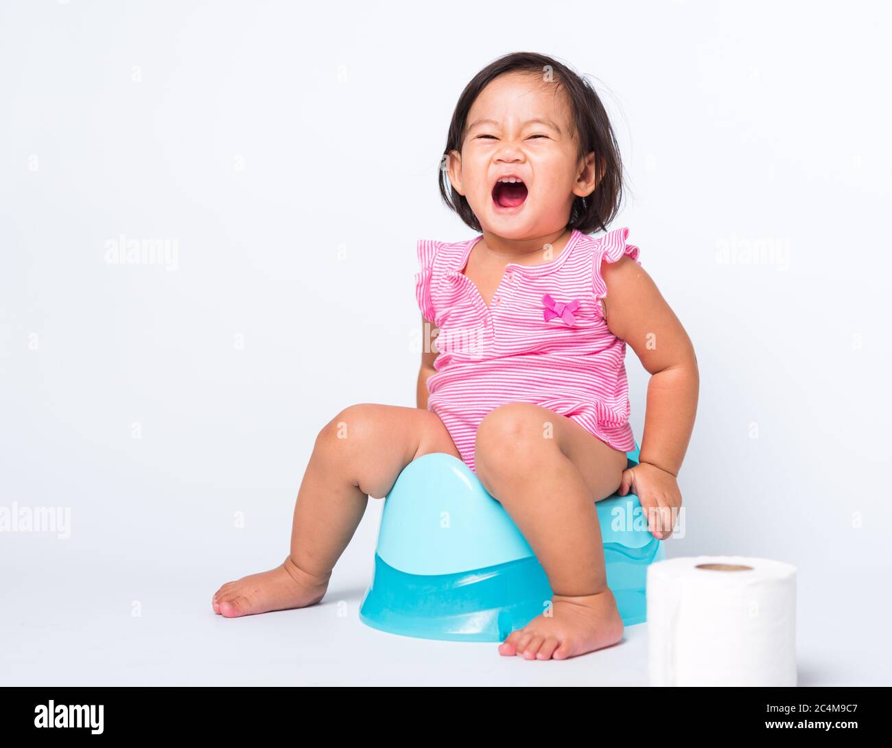 Asiatique petite mignonne bébé fille éducation entraînement à s'asseoir sur pot bleu de chambre ou pot avec des rouleaux de papier toilette, studio tourné isolé sur la ba blanche Banque D'Images
