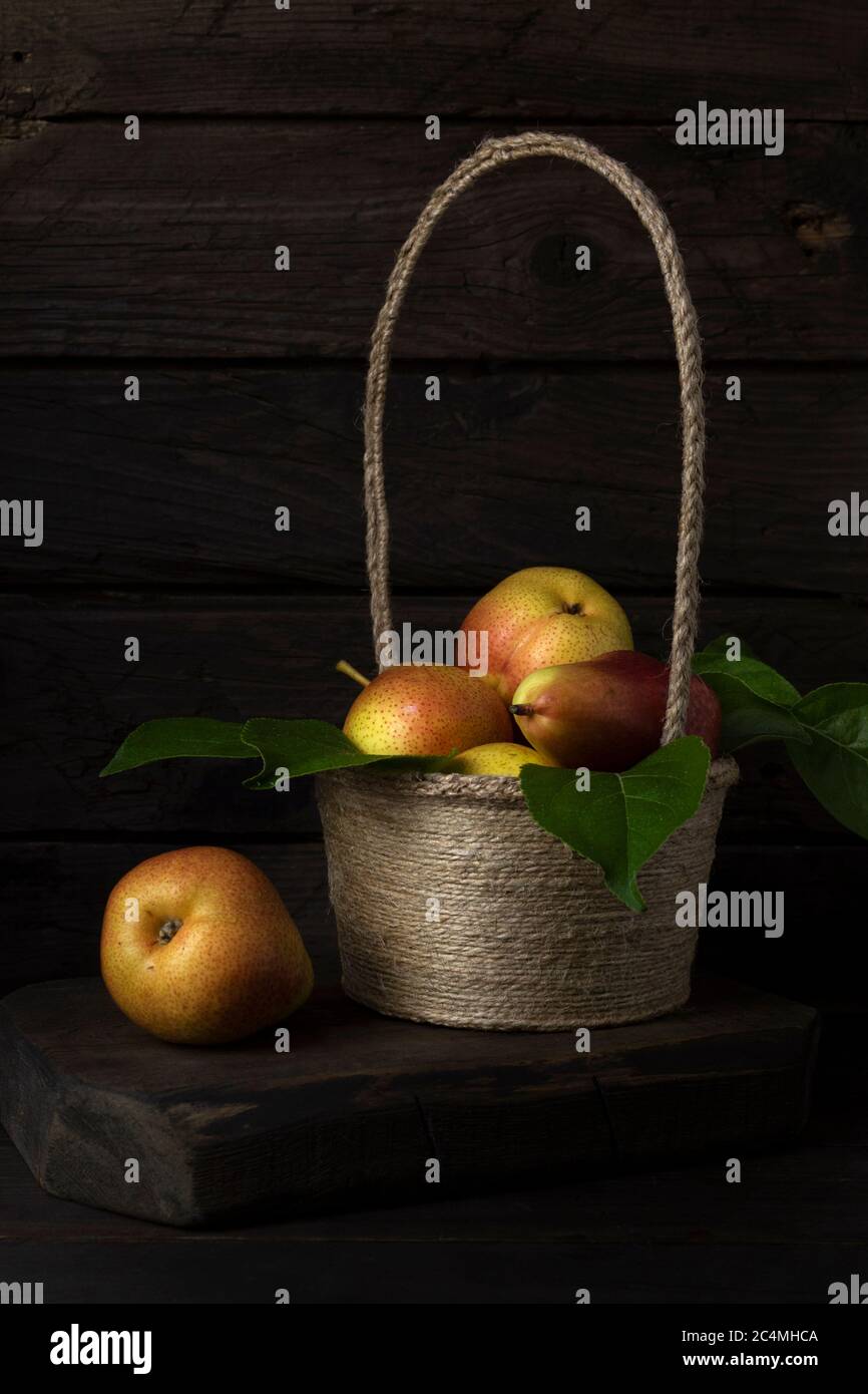 Panier avec poire aux fruits mûrs et feuilles vertes sur table en bois. Encore une vie dans un style rustique. Banque D'Images