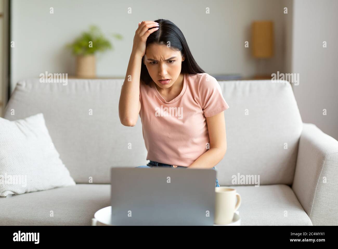 Une fille perplexe à l'ordinateur portable, à la tête de grattage assise sur le canapé à l'intérieur Banque D'Images