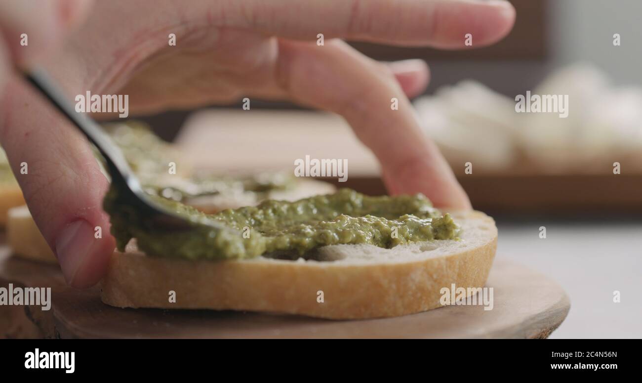 homme répandant du pesto sur une tranche de pain de ciabatta sur un plateau d'olive Banque D'Images