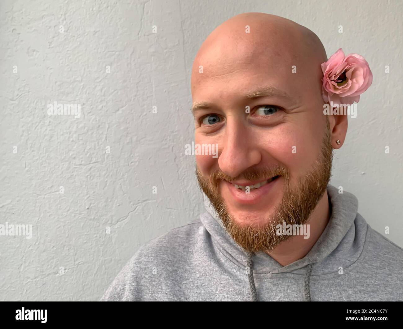 Jeune européen blanc beau sans cheveux fou souriant homme homme homme avec  barbe et fleur rose derrière son oreille Photo Stock - Alamy