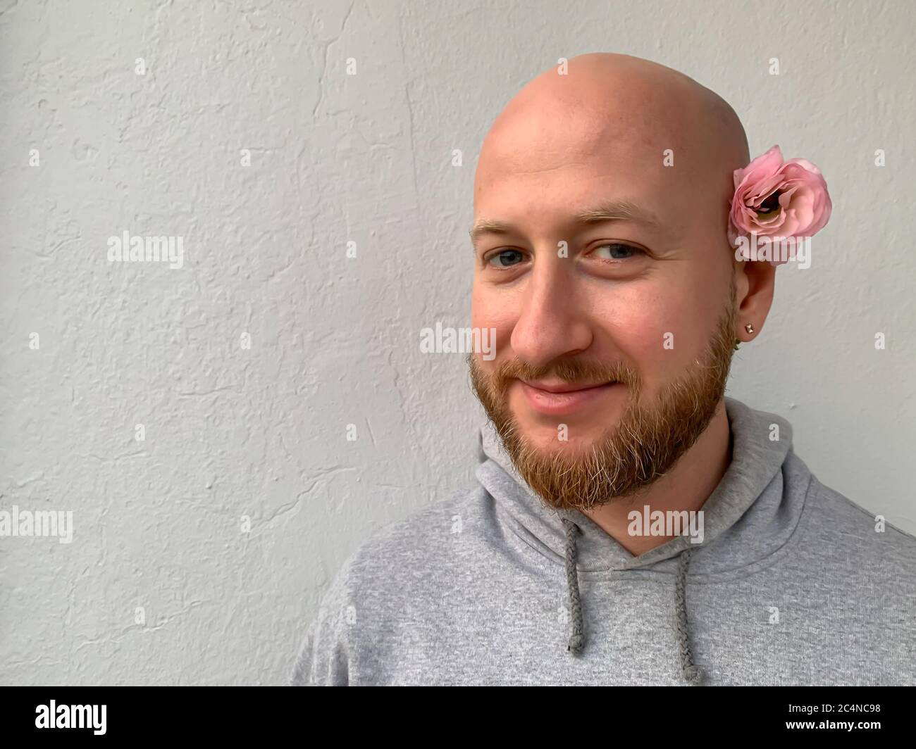 Jeune européen blanc beau sans cheveux chauve homme souriant homme homme  avec barbe et fleur rose derrière son oreille Photo Stock - Alamy