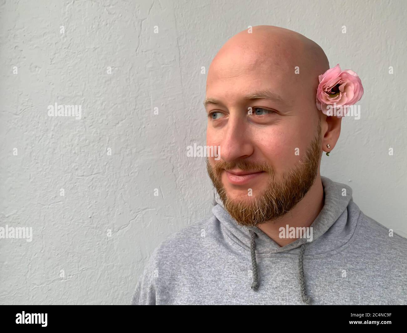 Jeune homme européen blanc beau sans cheveux homme homme avec barbe et  fleur rose derrière son oreille Photo Stock - Alamy