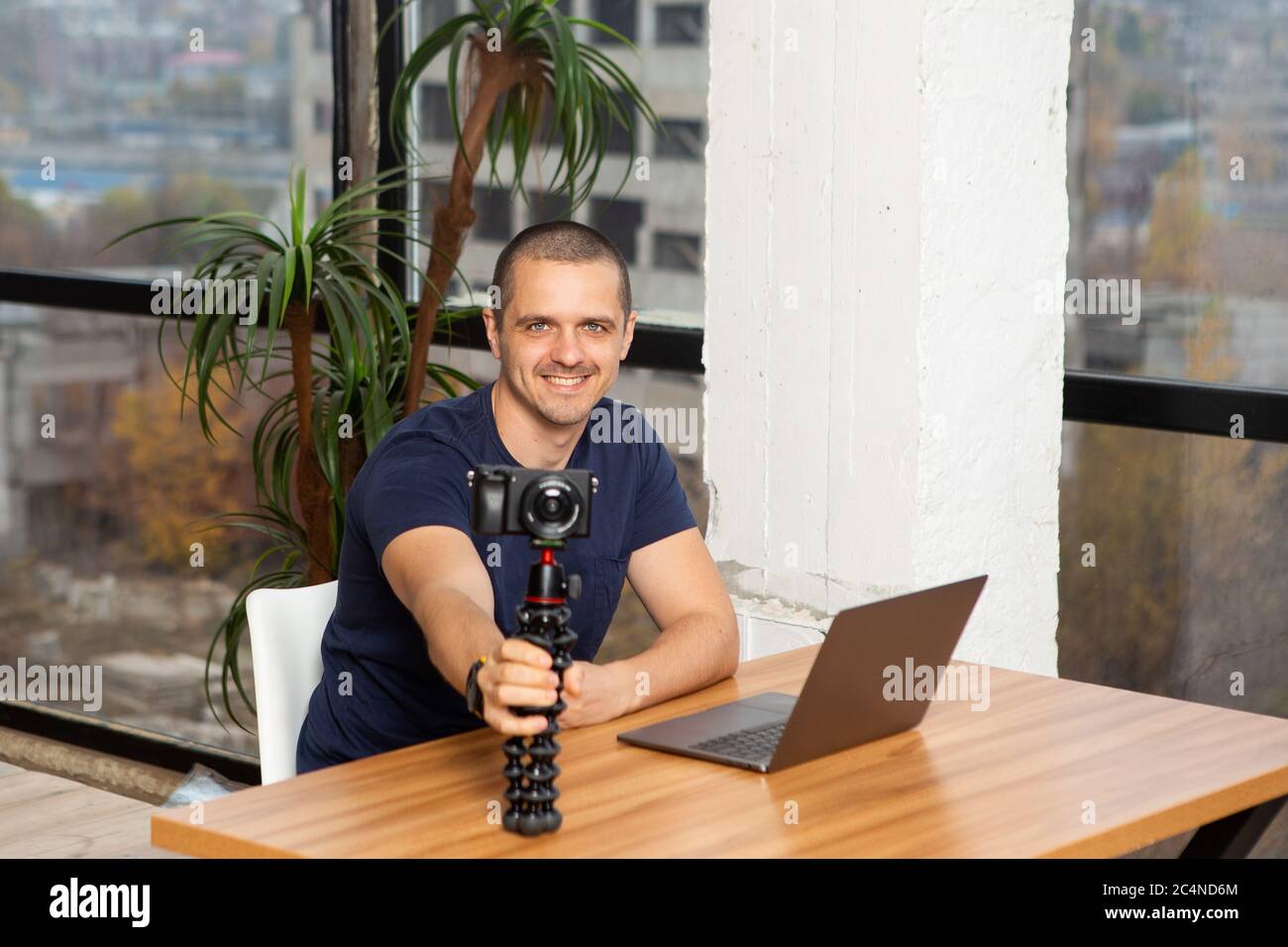 Homme blogueur vidéo tenant la caméra tout en étant assis à la table avec ordinateur portable Banque D'Images