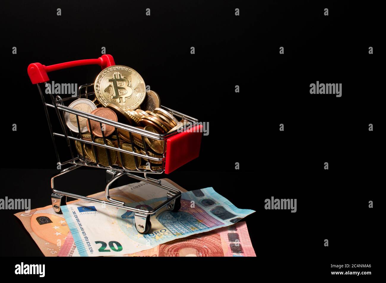 Panier miniature rempli de pièces en euros et d'un bitcoin sur le dessus placé sur l'argent papier avec un fond noir. Gagner de l'argent avec crypto curren Banque D'Images