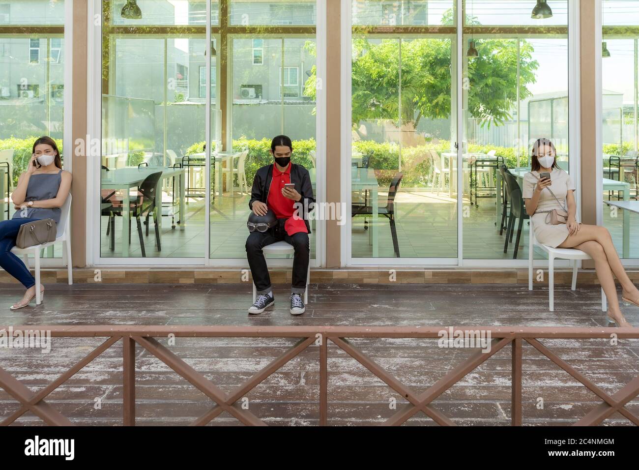 Les clients asiatiques portent un masque facial avec un téléphone mobile tout en s'asseyant dans la file d'attente de distance sociale devant le restaurant avec espace libre de rédaction pour le montage. Banque D'Images