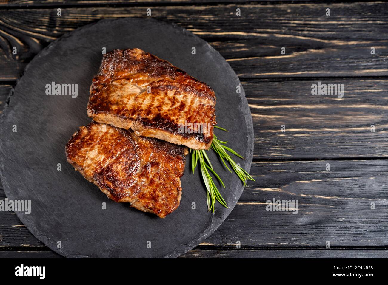 Un morceau juteux de viande frite se trouve sur une plaque de pierre contre une table en bois noir. Degré de torréfaction bien fait. Food concept with copy space Banque D'Images