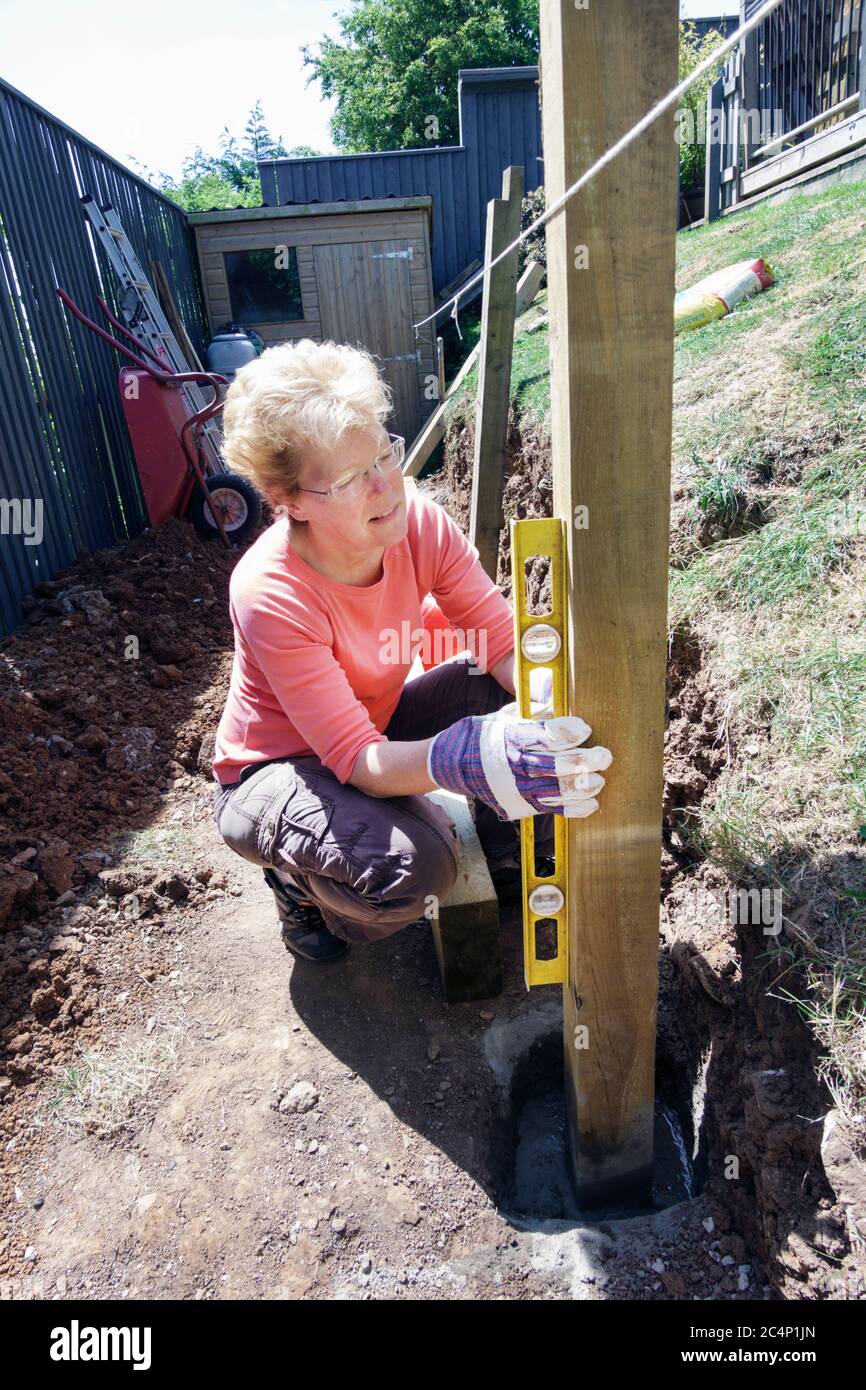 Une femme travaillant sur l'aménagement d'un jardin. Elle place des poteaux en bois dans le sol en utilisant un niveau à bulle pour s'assurer que le poteau est bien droit Banque D'Images