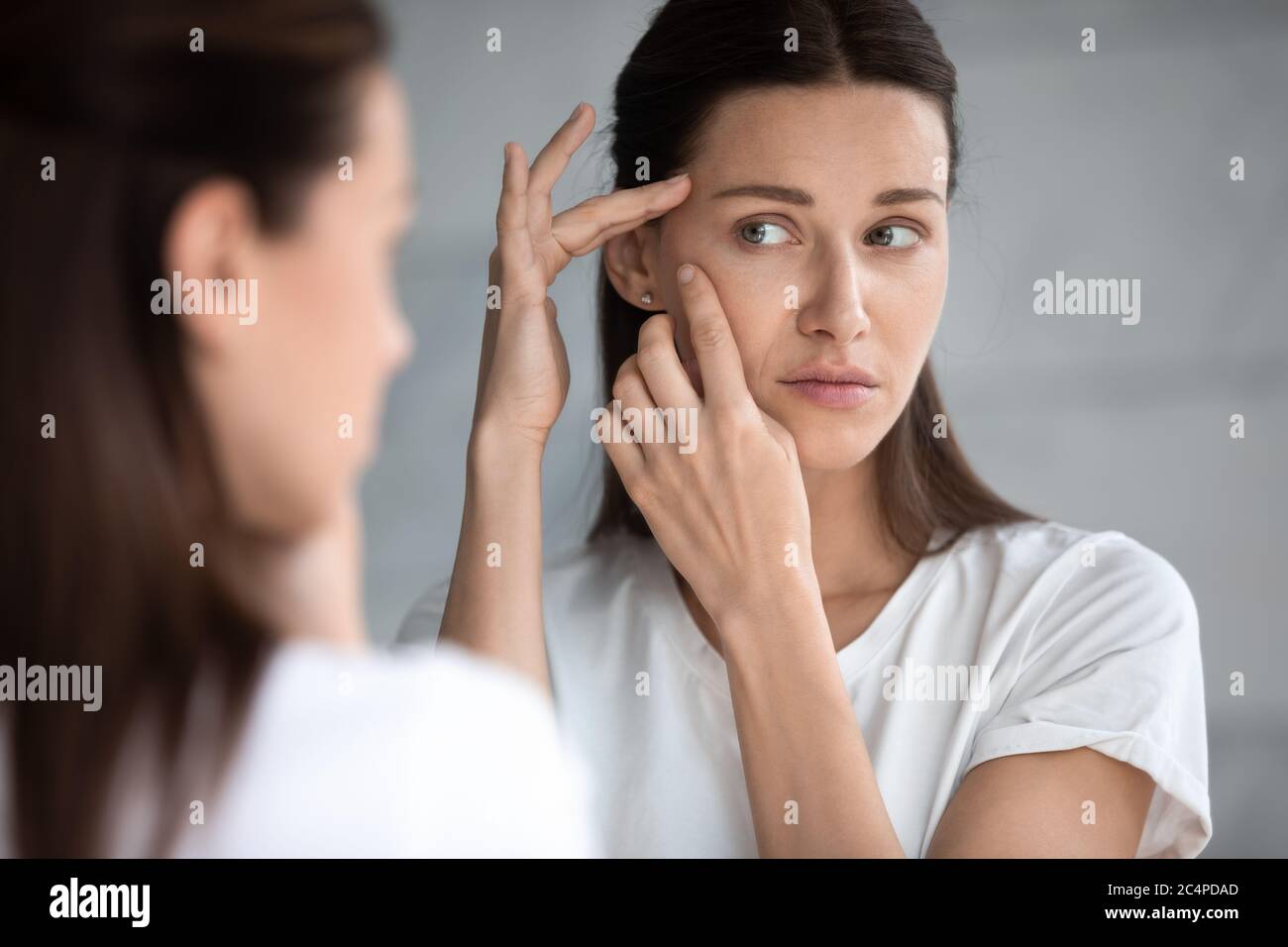 Femme anxieux jeune regarder dans le miroir inquiet au sujet de l'acné de visage Banque D'Images