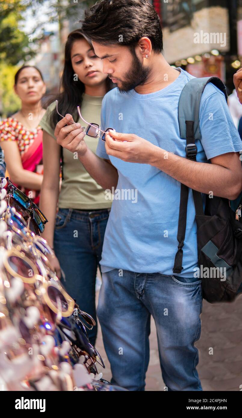 Jeune Indien qui choisit et achète des lunettes de soleil sur le marché  extérieur de la rue avec la famille à l'heure du jour. Lieu de tournage  Sarojini Nagar, delhi, Inde.Indien Photo