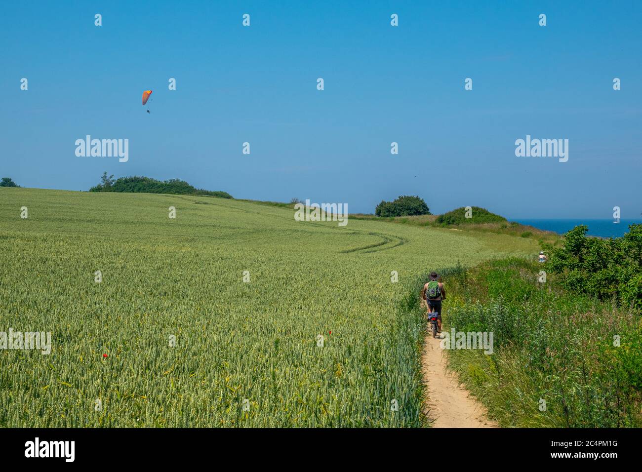 un cycliste suit un chemin de sable très étroit et un parapente vole à l'horizon Banque D'Images