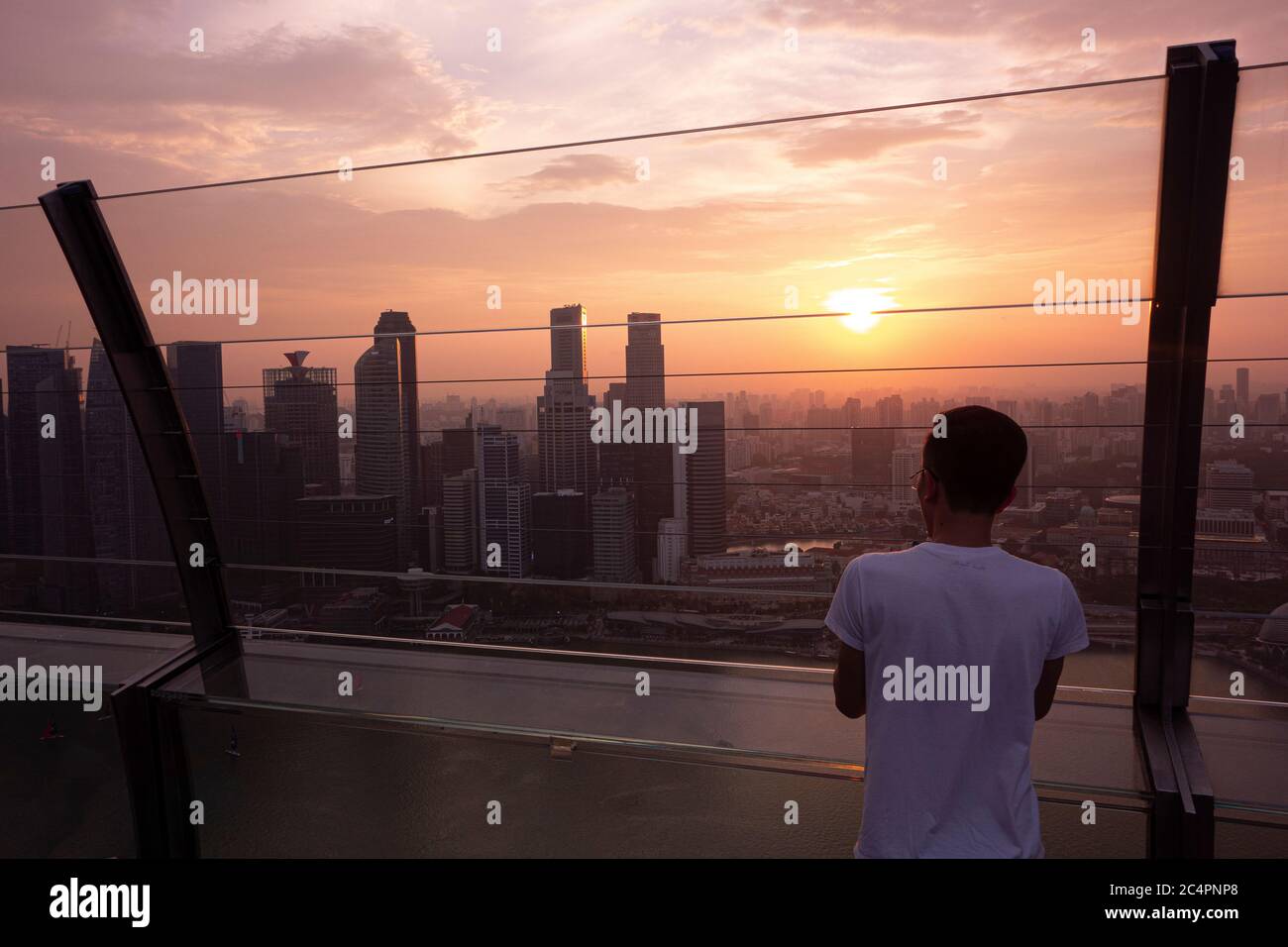 Jeune homme observant le coucher de soleil sur la ligne d'horizon du centre-ville de Singapour, vu de Marina Bay Sands. Singapour Banque D'Images