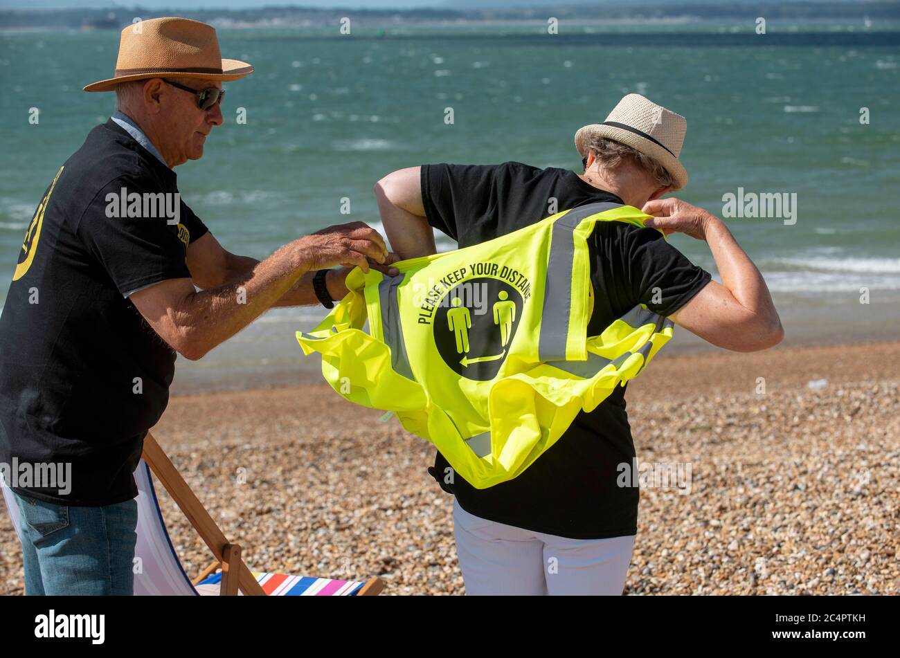 Southsea, Hampshire, Angleterre, Royaume-Uni. Juin 2020. Homme aidant la femme à porter un t-shirt social et à garder votre distance hi vis gilet Banque D'Images