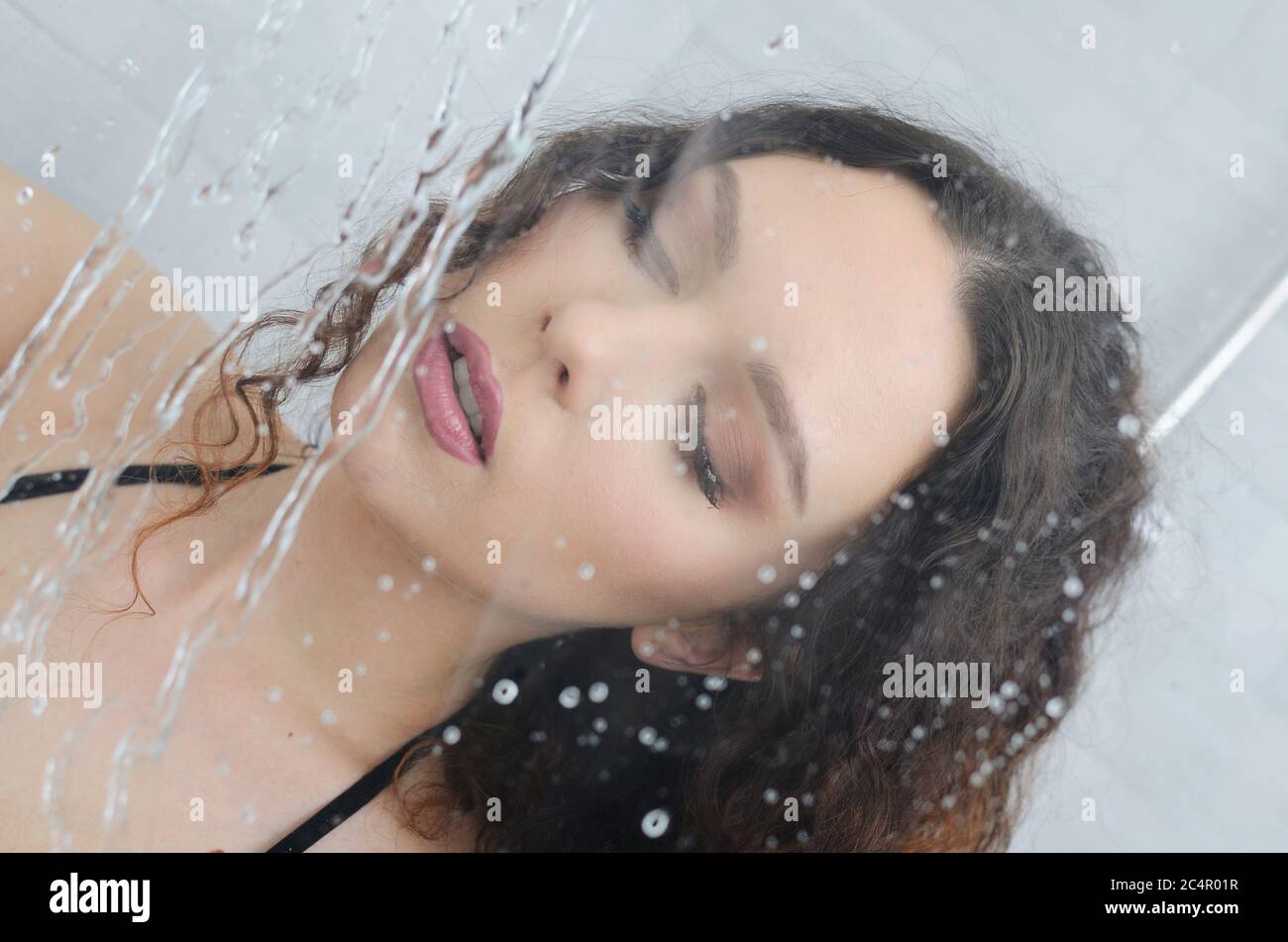 Fille sous la douche avec jet d'eau devant son visage. Jeune femme séjournant dans son appartement. Banque D'Images
