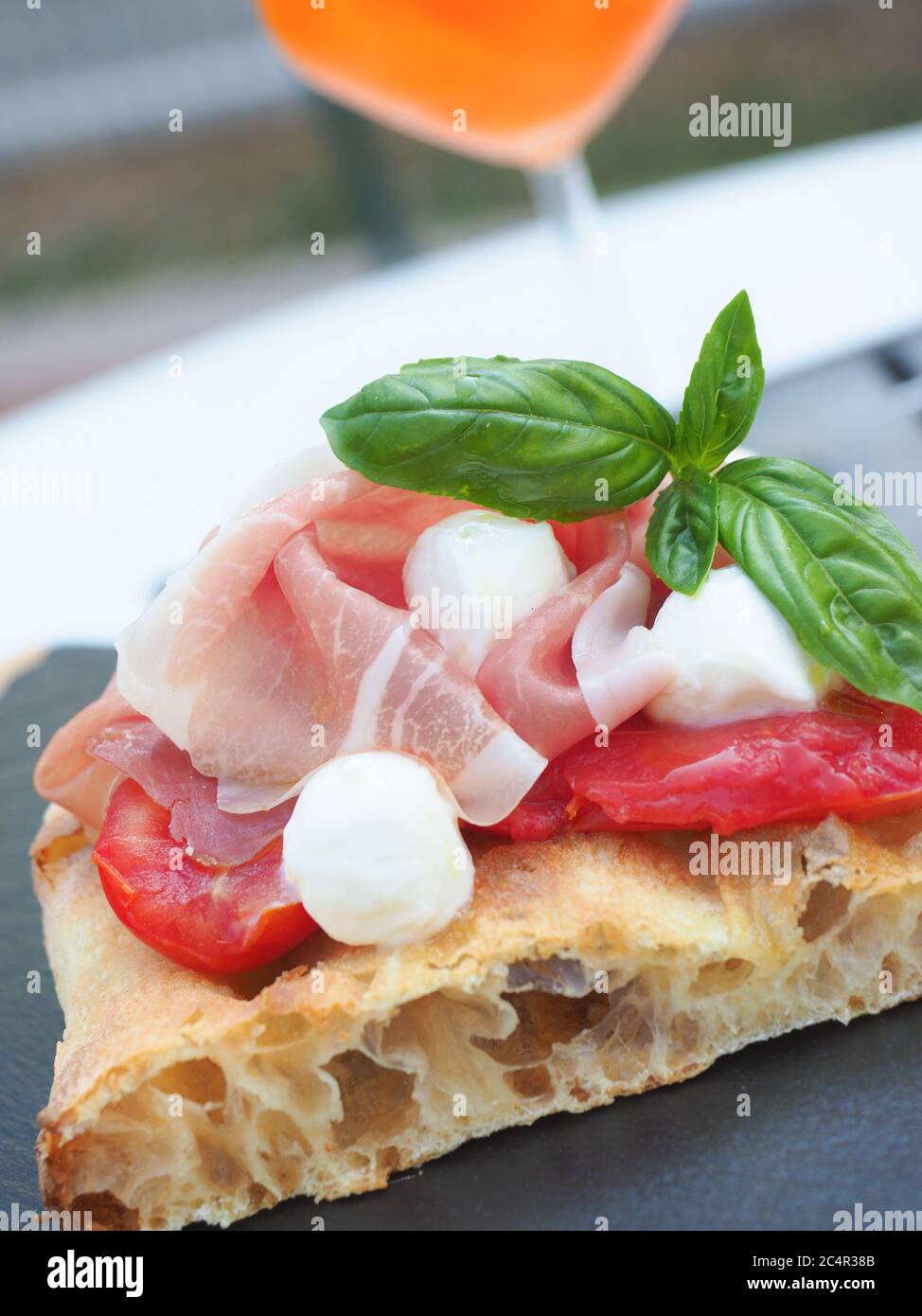 Tranche de pain de focaccia romana habillé de parme ha, de tomate, de mozzarella et de basilic frais. Verre de spritz italien sur fond Banque D'Images