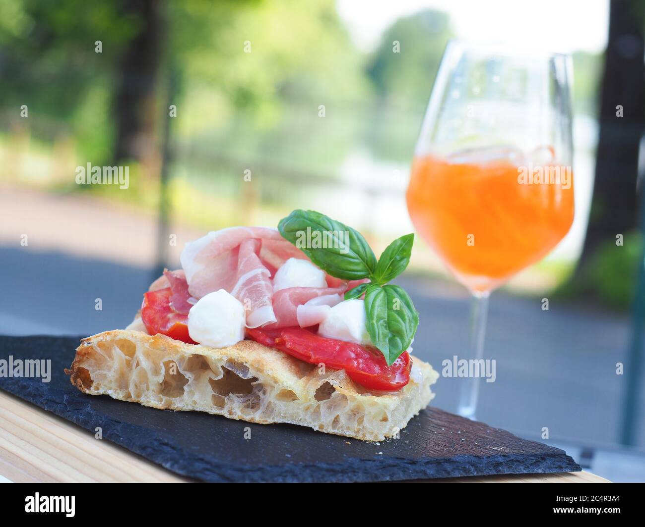 Tranche de pain de focaccia romana habillé de parme ha, de tomate, de mozzarella et de basilic frais. Verre de spritz italien sur fond Banque D'Images