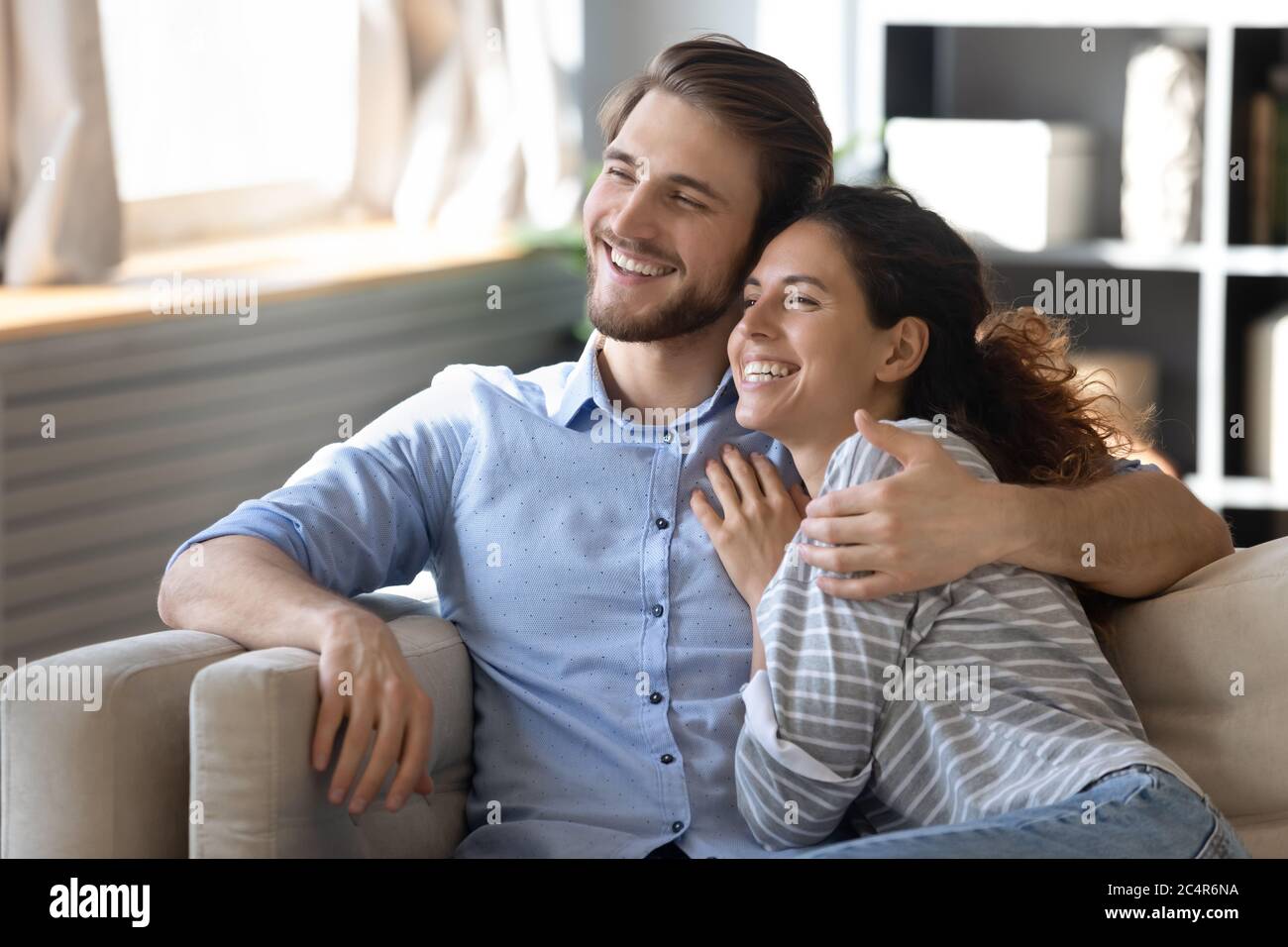 Femme et homme souriant rêveux se embrassant, se reposant sur un canapé confortable Banque D'Images