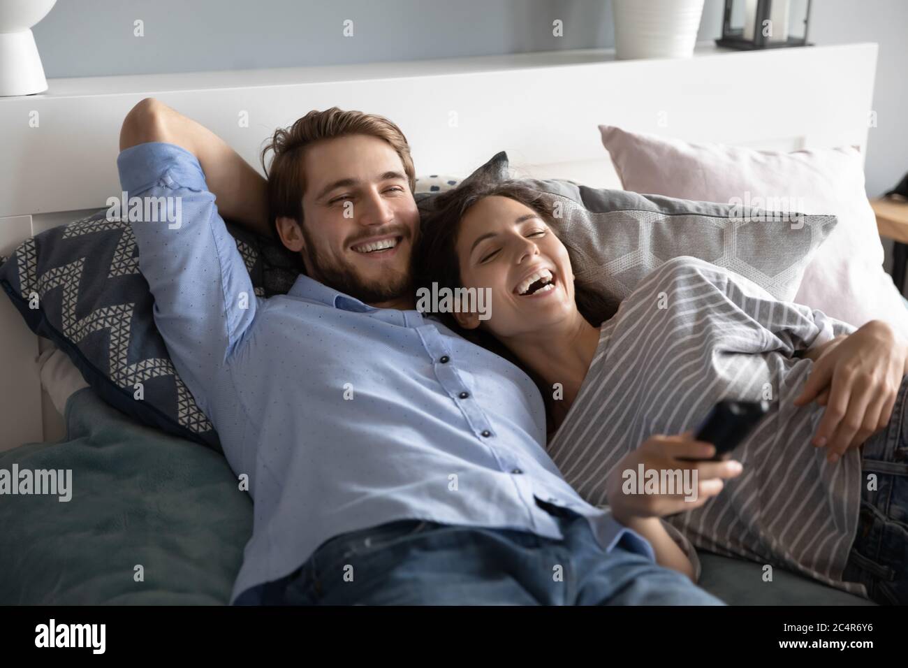 Rire homme et femme allongé dans le lit, regardant la télévision Banque D'Images