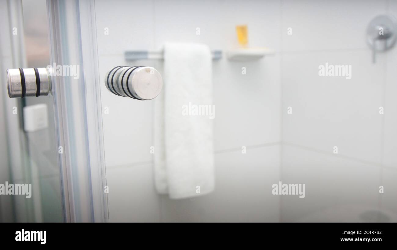 Salle de bains avec portes en verre et murs en céramique blanche avec serviette et shampooing à l'intérieur Banque D'Images