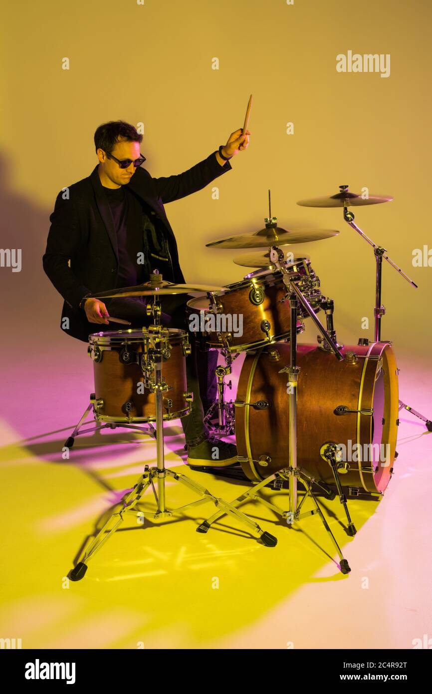 Batteur mâle caucasien improvisant isolé sur fond de studio léger dans la lumière de néon. Performances, look inspiré, énergie. Banque D'Images