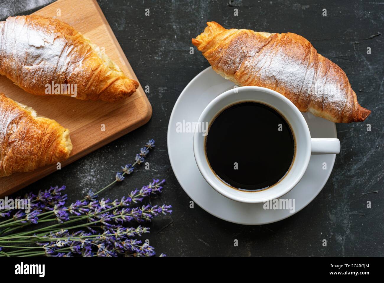 Une tasse de café et croissants, bouquet de fleurs de lavande sur table noire, vue sur le dessus. Concept petit déjeuner Banque D'Images
