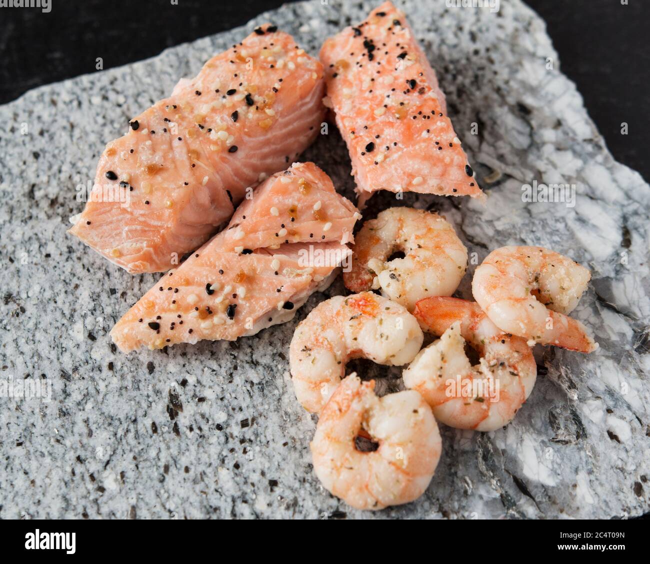Crevettes et saumon rôdés avec tout l'assaisonnement à bagel sur une planche à découper en granit et un fond en ardoise noire. Banque D'Images