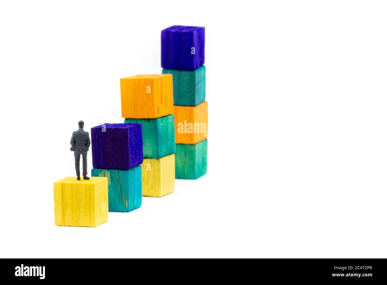 Figurine miniature posée comme homme d'affaires assis seul sur un cube en bois regardant vers les piles colorées comme un business Chart, concept abstrait minimaliste i Banque D'Images