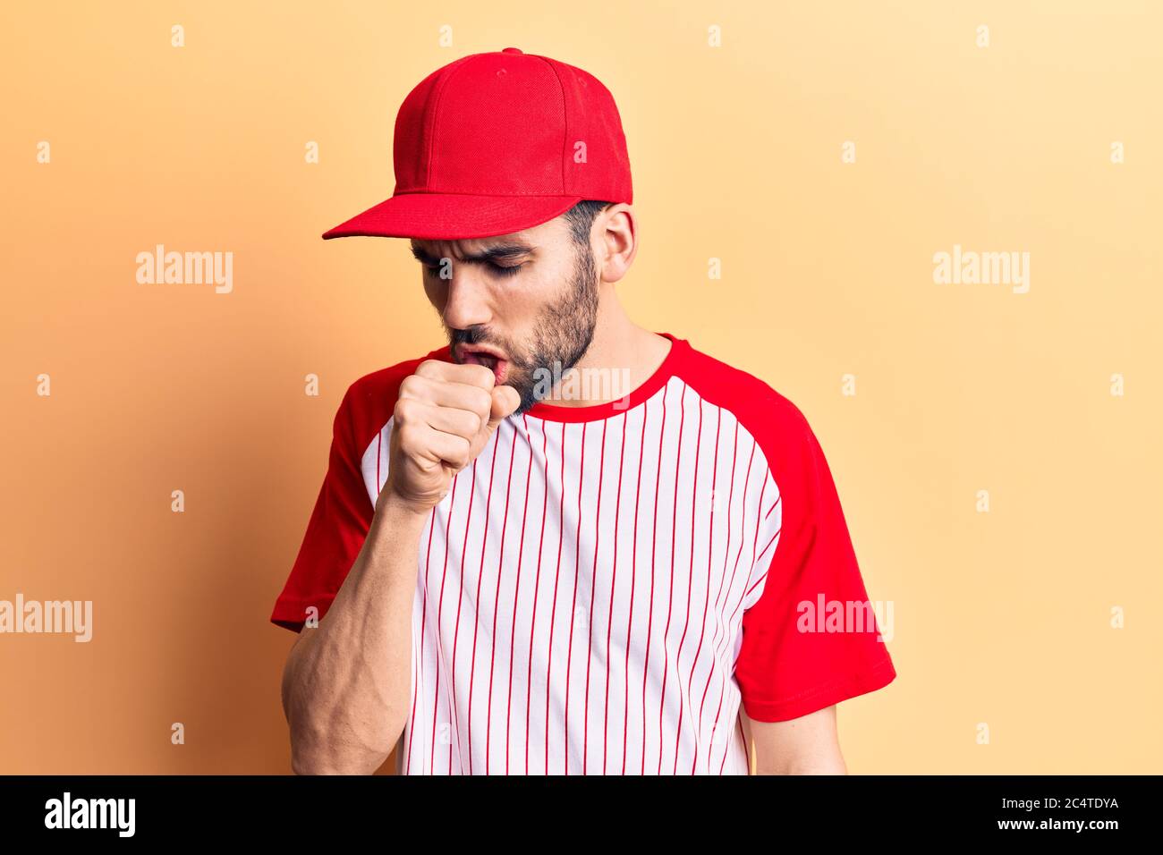 Jeune homme beau avec barbe portant une casquette de baseball et un t-shirt  se sentant mal et toussant comme symptôme de rhume ou de bronchite. Concept de  soins de santé Photo Stock -