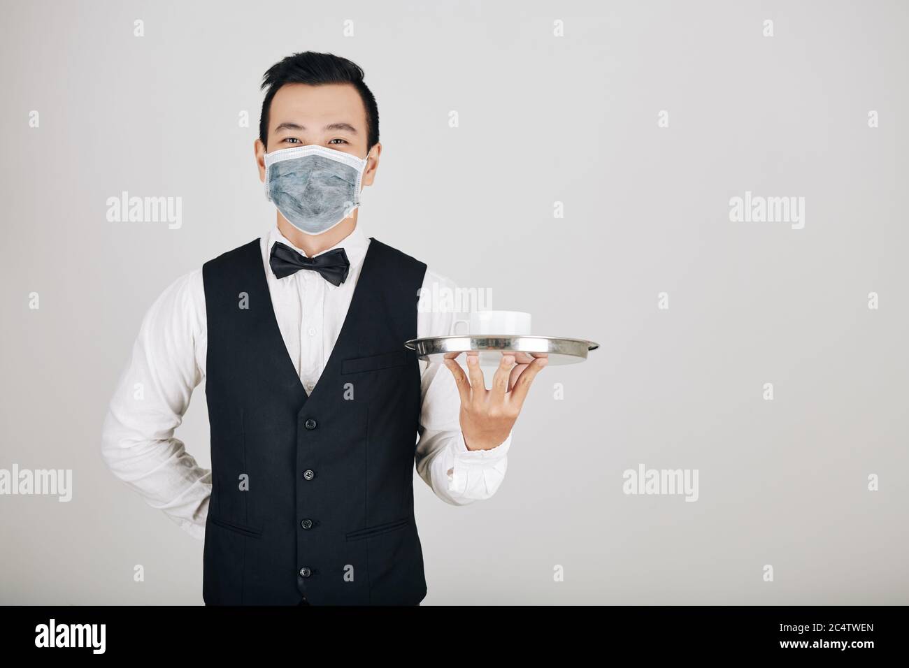 Portrait d'un jeune serveur souriant dans un plateau de rangement pour masque médical avec bol de soupe Banque D'Images