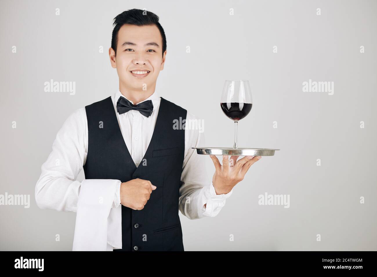 Jeune serveur positif avec serviette blanche et verre de vin rouge sur plateau métallique Banque D'Images