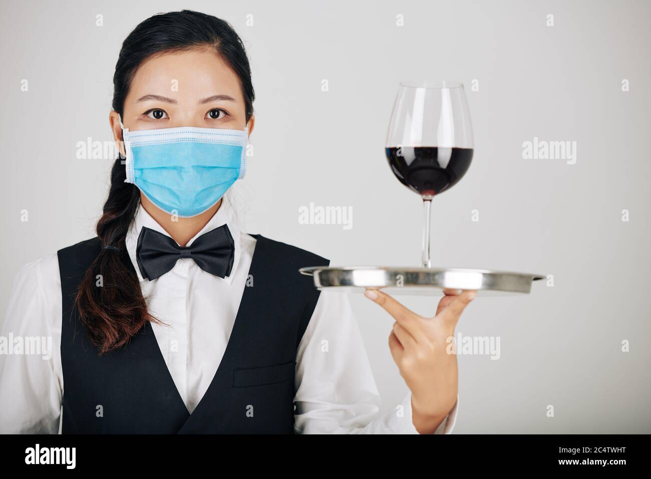 Portrait d'une jeune serveuse vietnamienne sérieuse dans un plateau de vin médical avec un verre de vin rouge Banque D'Images