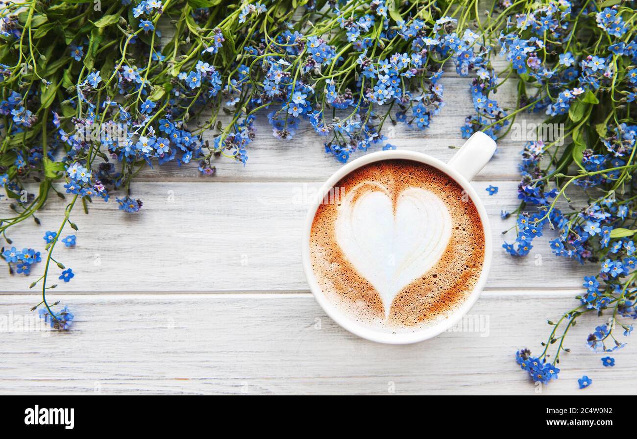 Fleurs bleues oubliées et une tasse de café chaud sur une table en bois blanc Banque D'Images