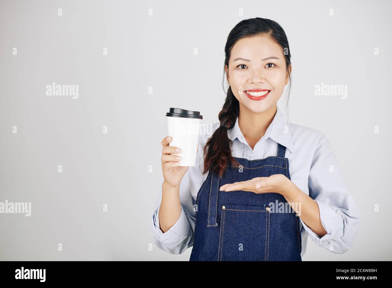 Portrait de la jeune femme souriante propriétaire de café montrant une tasse de café à emporter le café qu'elle a fait pour la cliente Banque D'Images