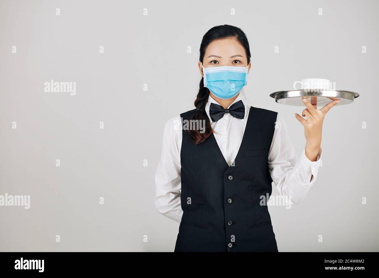 Portrait de la serveuse yuong sérieuse dans un plateau de transport de masque médical avec un bol de soupe Banque D'Images