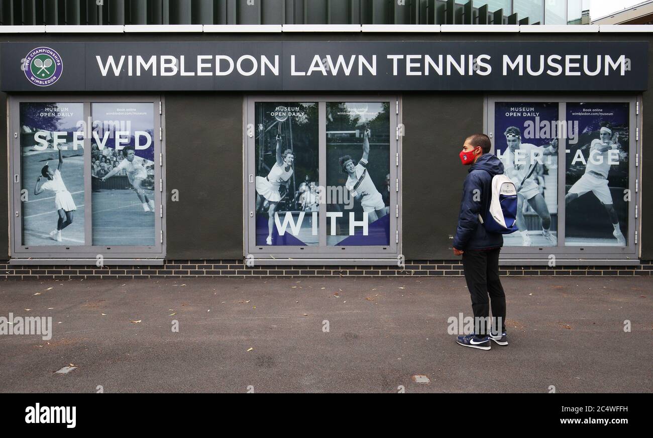 Un fan de tennis portant un sac de dos de marque Wimbledon et un masque rouge se tient devant le All England Lawn tennis and Croquet Club, Wimbledon, à l'occasion de ce qui aurait été le premier jour du célèbre tournoi de tennis, qui a été annulé cette année en raison de la menace du coronavirus. Banque D'Images