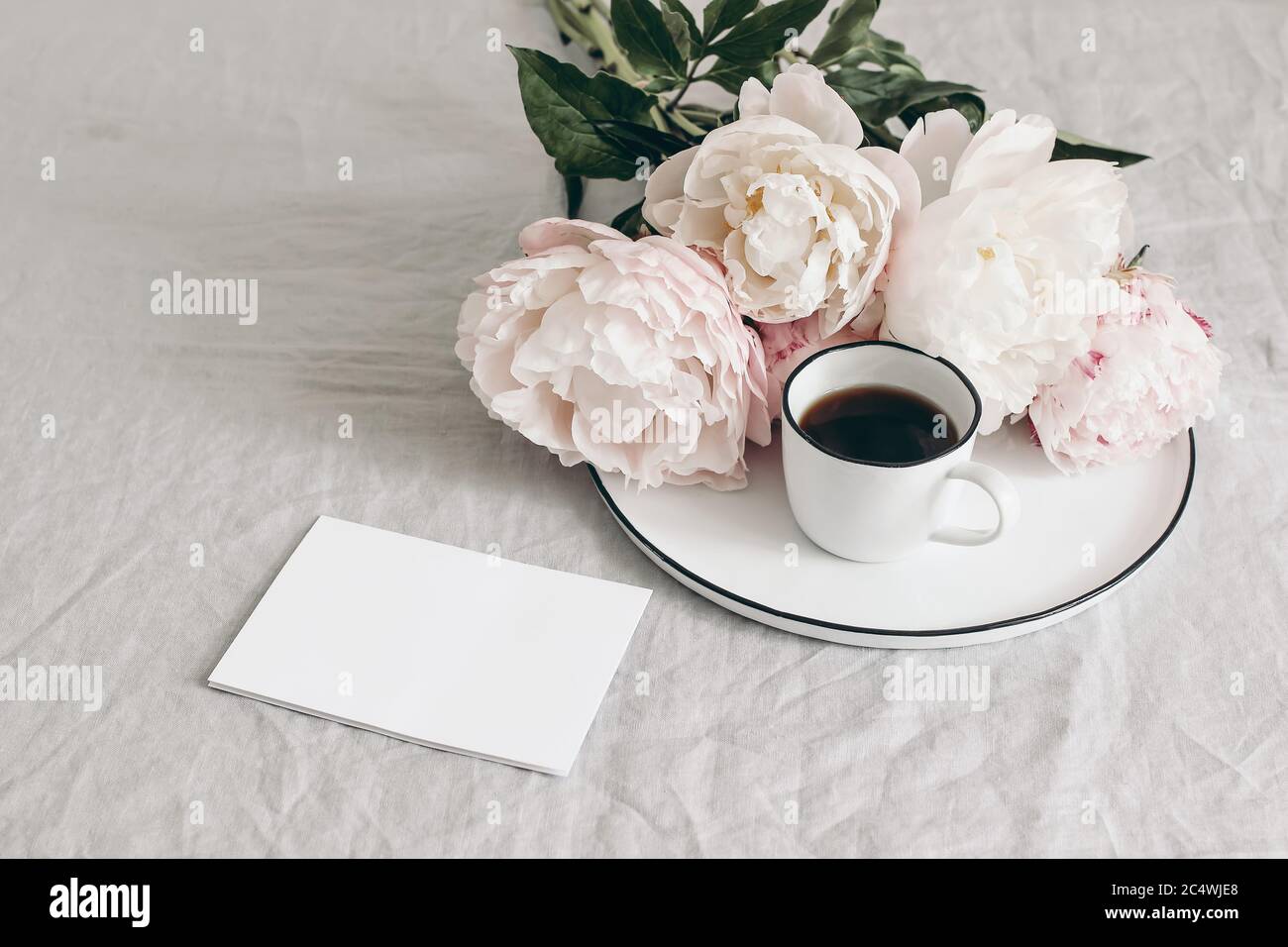 Le petit déjeuner de printemps encore la scène de vie. Tasse de café et bouquet de pivoines blanches et roses sur plaque en porcelaine. Carte de vœux vierge maquette sur table en lin Banque D'Images