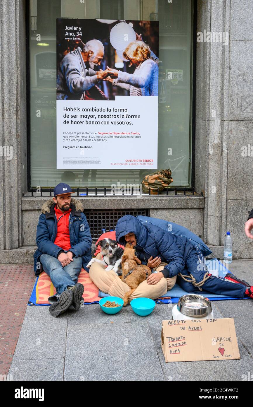 Les hommes sans abri implorent leurs chiens, en dessous d'une publicité bancaire dans le centre de Madrid, en Espagne. Banque D'Images