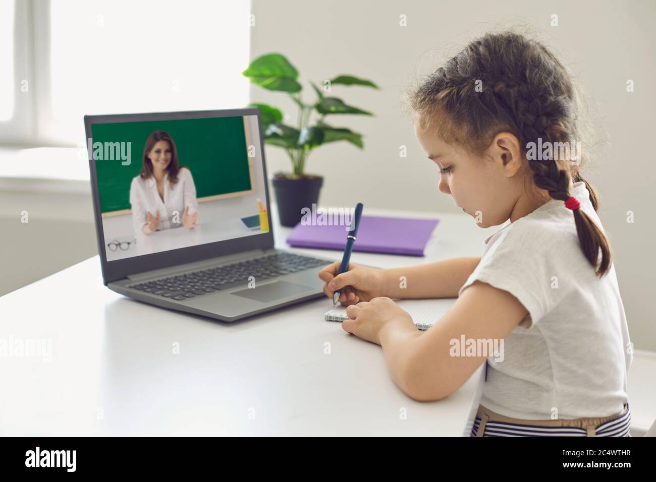 Éducation scolaire en ligne. Une petite fille une écolière écrit dans un bloc-notes a une leçon vidéo avec une femme enseignant d'ordinateur portable à la maison. Banque D'Images