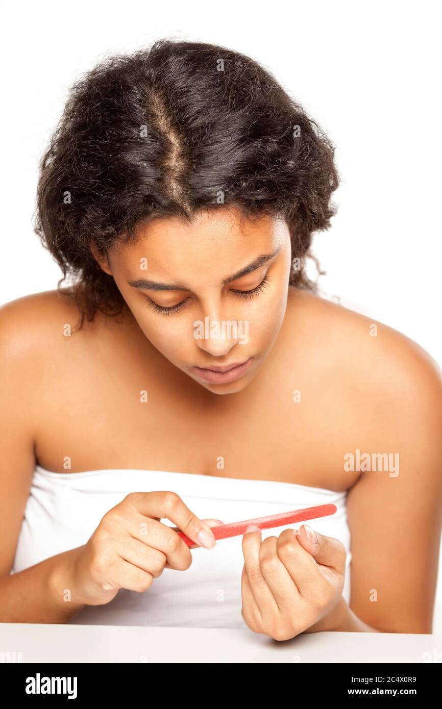 Jeune femme à la peau foncée remplissant ses ongles de doigt sur fond blanc Banque D'Images